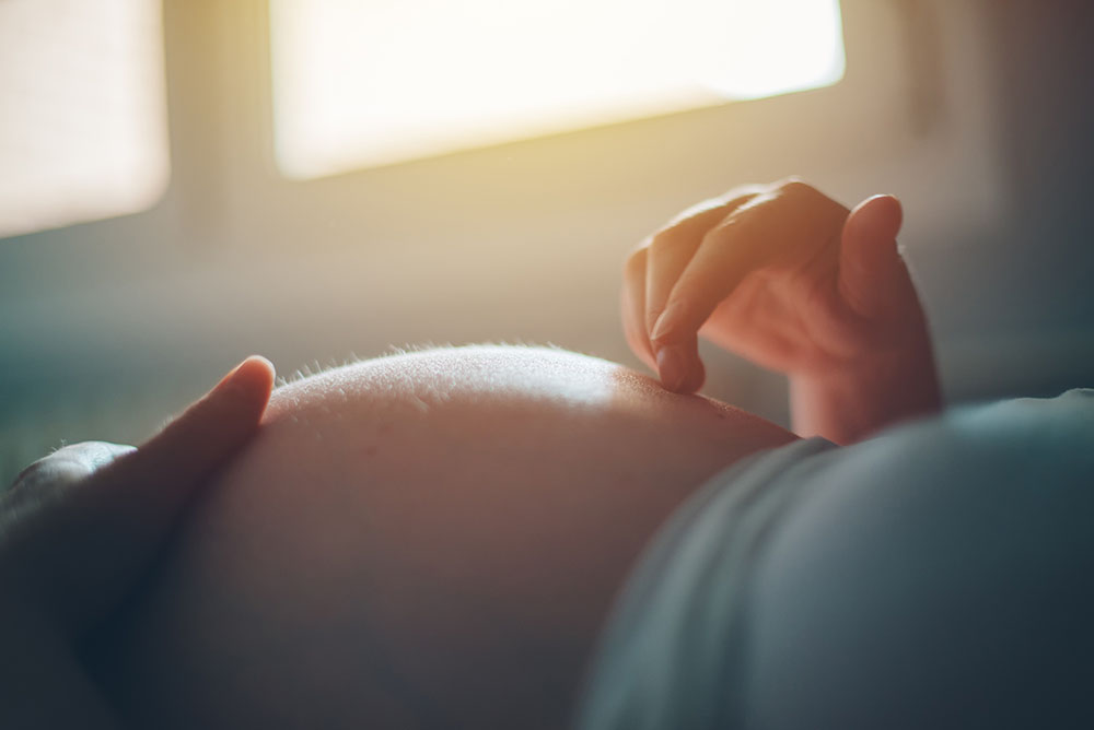 A woman runs her finger along her pregnant belly.