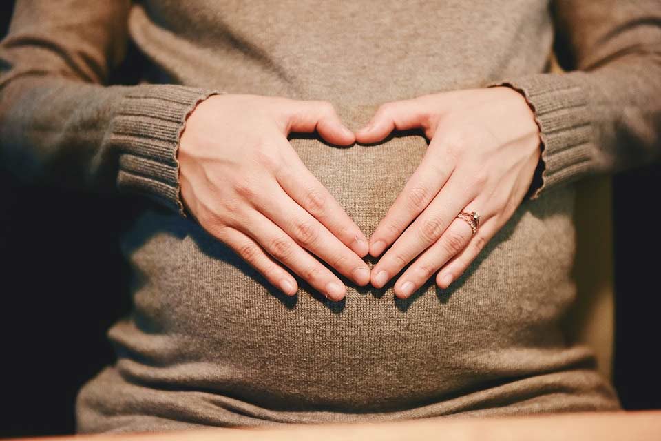A pregnant woman with her hands on her tummy in the shape of a heart.