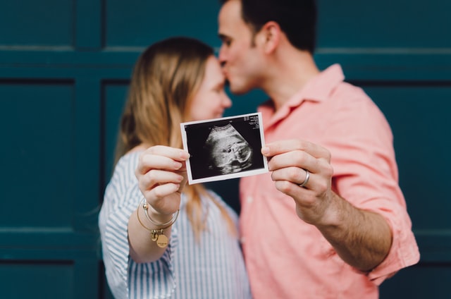 a kissing couple holding a sonogram image of their child