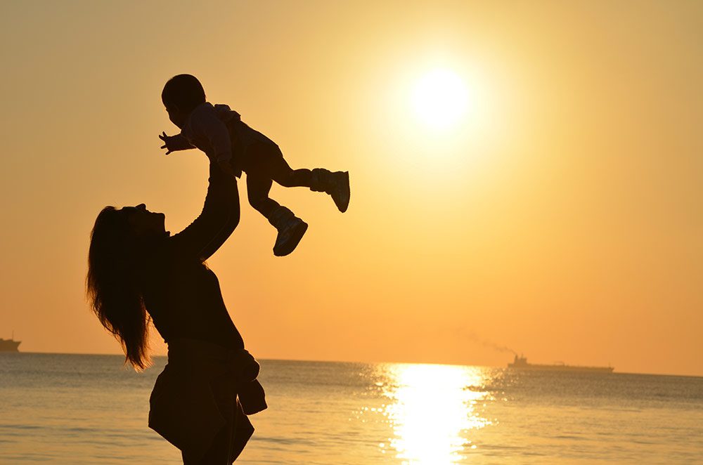 A woman holds an infant at the beach.