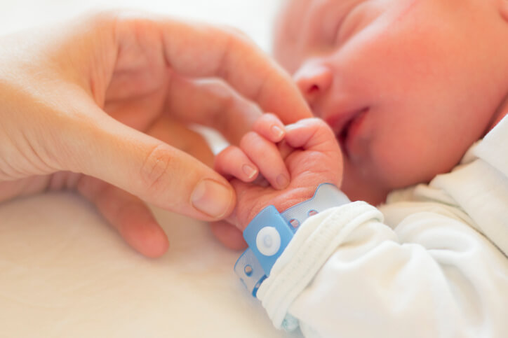 a newborn baby holding an adult’s hand