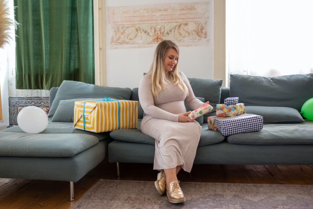 Pregnant woman sitting on couch receiving gifts