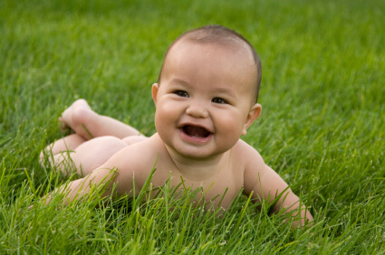 A smiling baby lies on green grass.