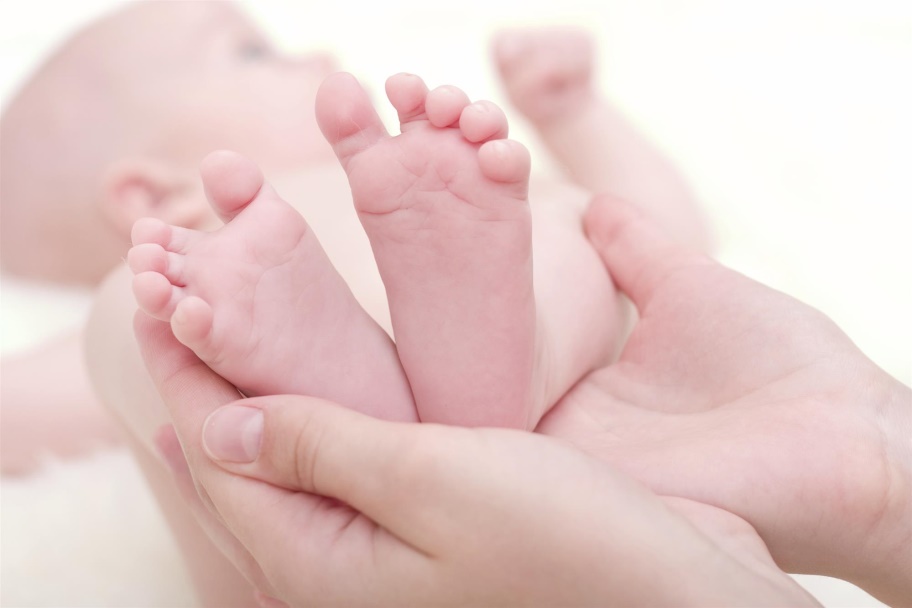 A surrogate mom holds a newborn baby’s feet.
