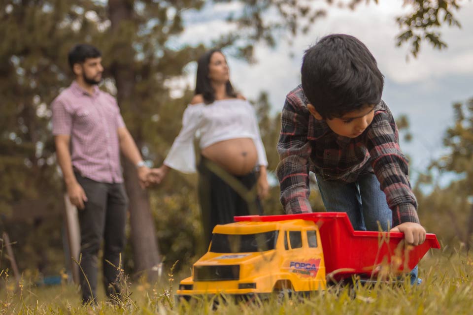 A boy plays with a toy truck while his father & pregnant mother watch