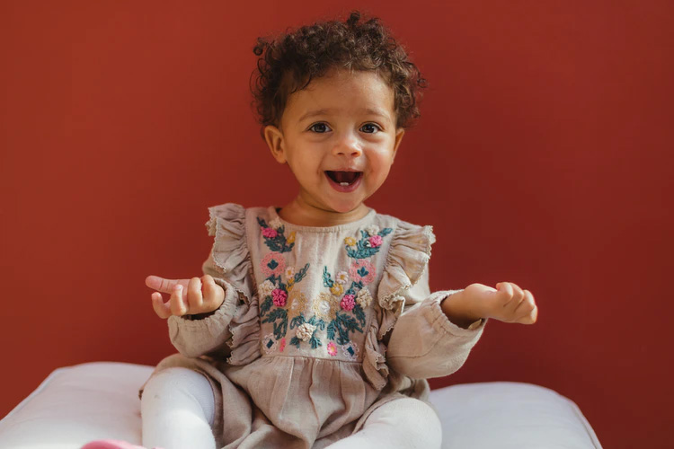 a curly-haired baby wearing a dress with floral embroidery