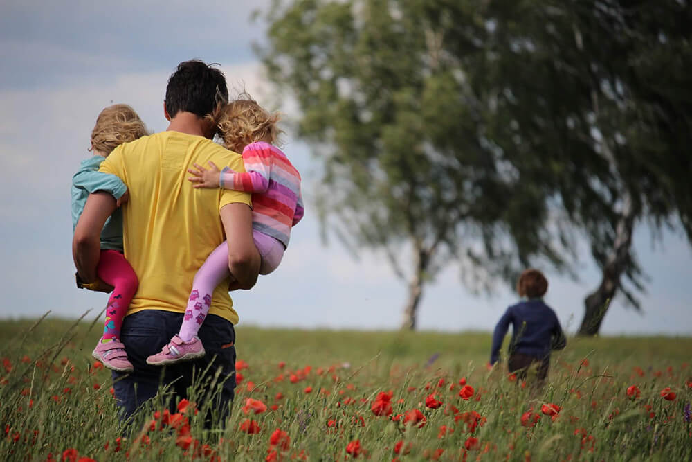 a father walking through a field with his three kids