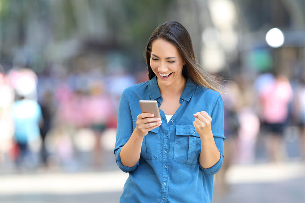 A happy woman in blue looking at her phone