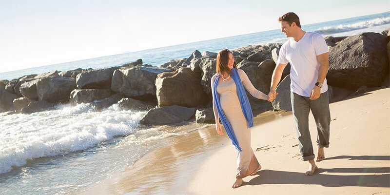 A man and a pregnant woman walking on the beach holding hands.