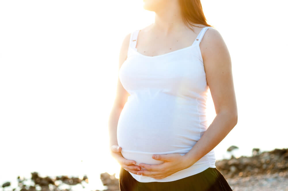 a pregnant woman holding her belly in the sunlight