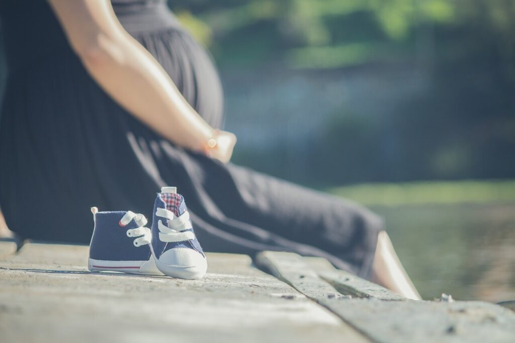 pregnant woman on a pier with baby shoes