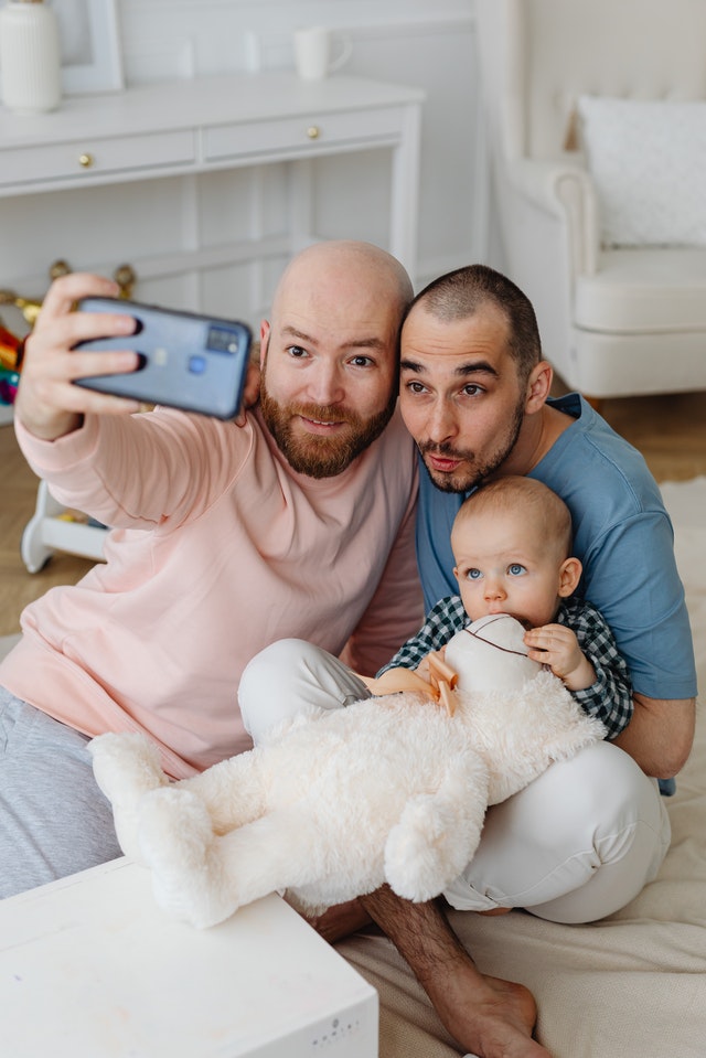 two men holding a baby and a teddy bear taking a picture