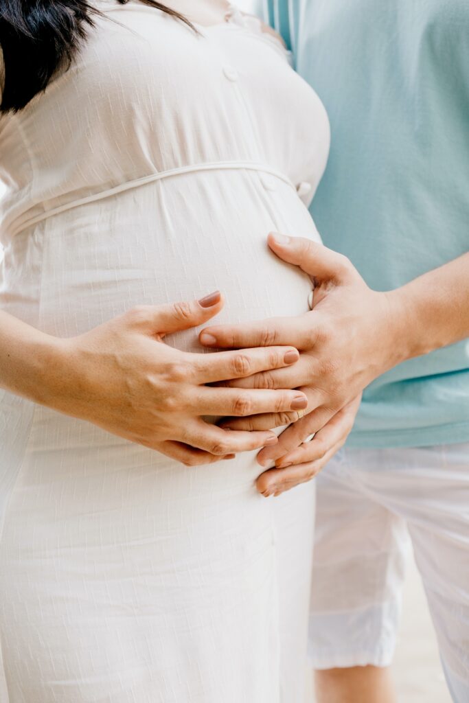 A man and woman place their hands on a surrogate’s pregnant belly