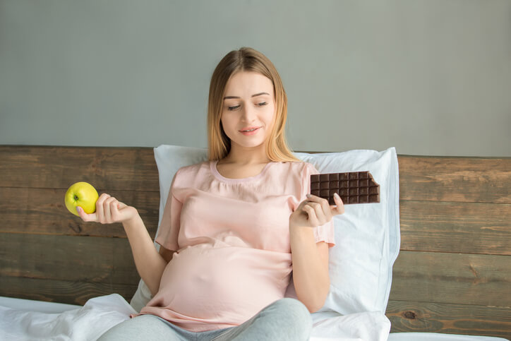 Pregnant woman with an apple in one hand and a chocolate bar in the other.
