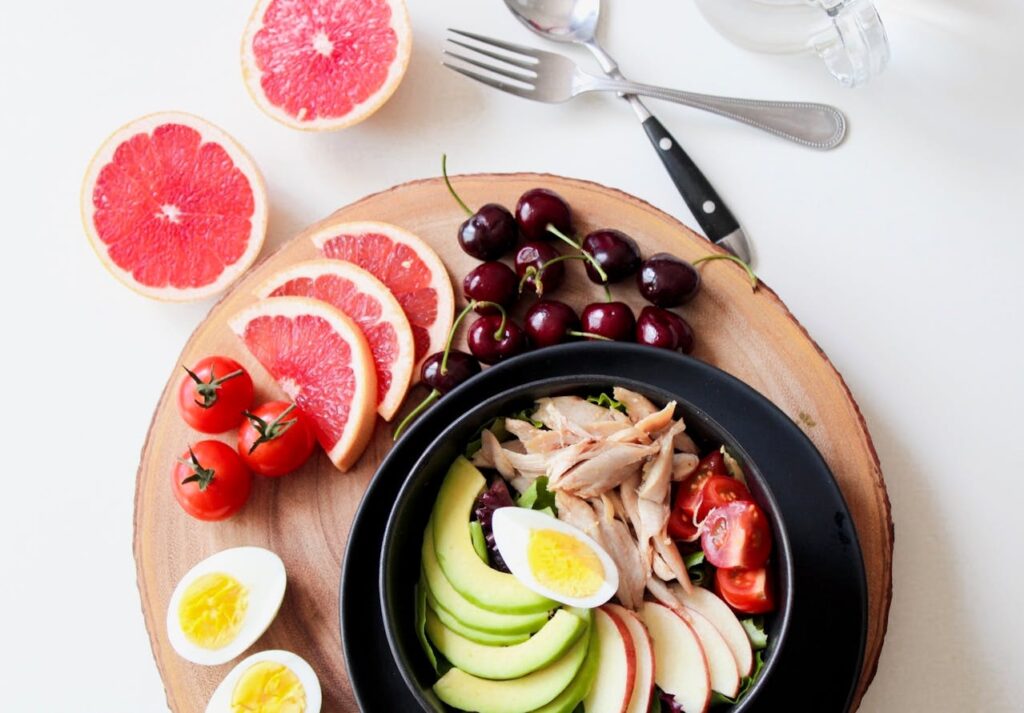 A platter of the best foods to eat during pregnancy: grapefruit, cooked eggs, avocado, cherries, apples, lean chicken, tomatoes, and leafy greens.