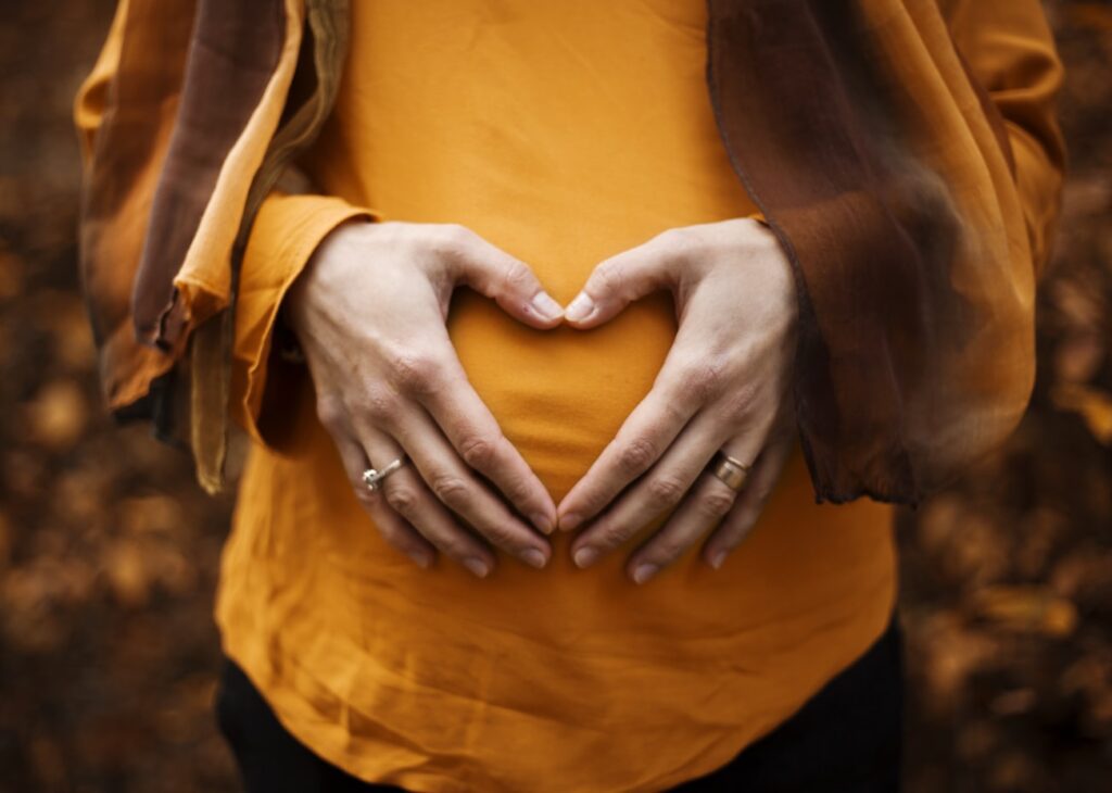 Hands form a heart shape over a surrogate mother’s belly.