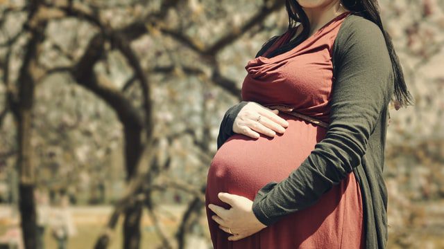 A surrogate mother tenderly holds her pregnant belly.