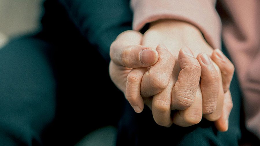 Photo of a couple holding hands, fingers intertwined.