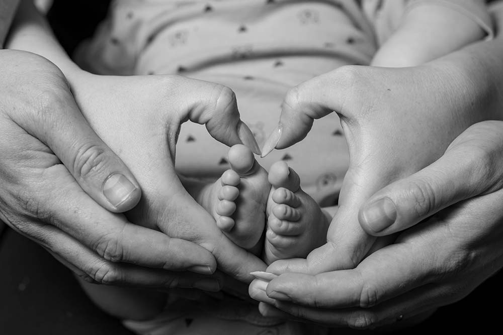 Parents making a heart with their hands around the baby’s feet.