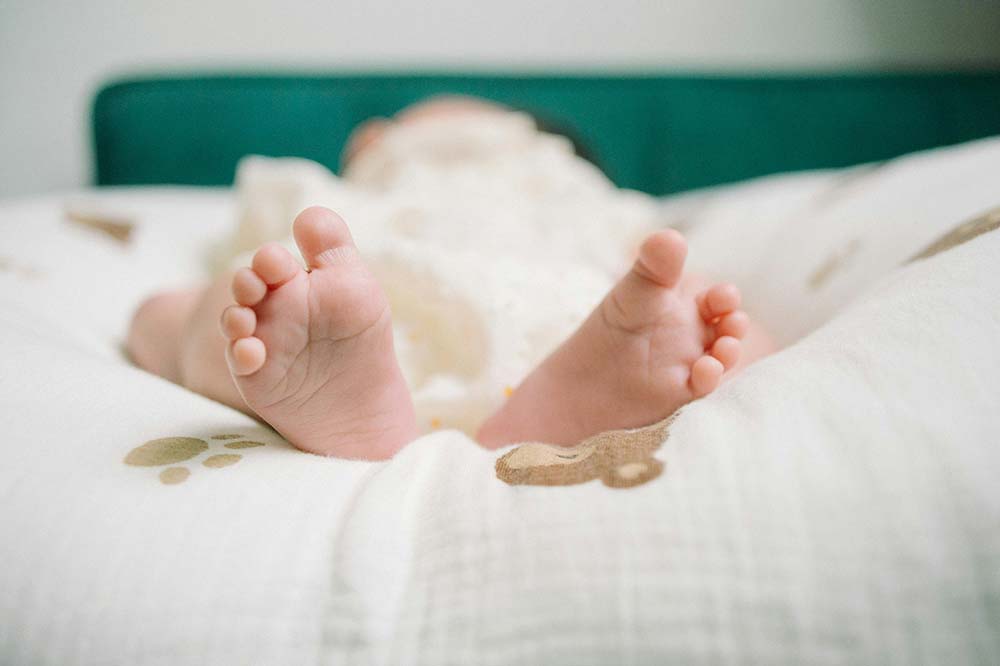 A baby lying on a bed with its soft, cute feet facing the camera.