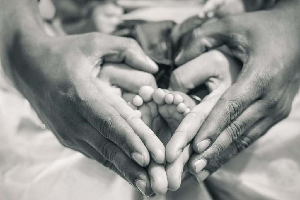 Parents' hands cradling their new baby’s feet in the shape of a heart