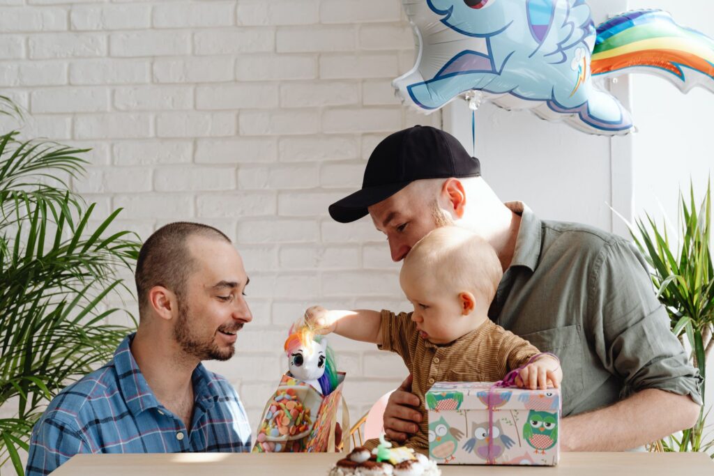Two LGBTQ+ parents with their young baby playing with a pony and giving the baby a gift.